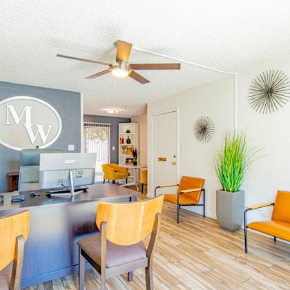 a living room with a desk and chairs and a ceiling fan