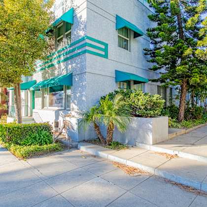 a white apartment building with green awnings and trees on a sidewalk
