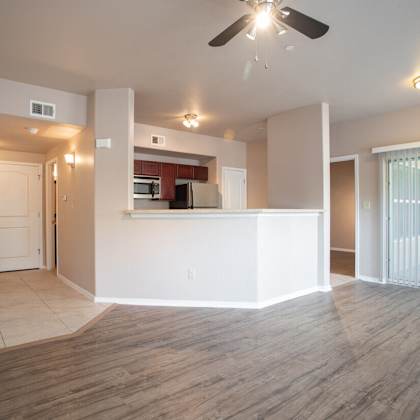 an empty living room with a ceiling fan and a kitchen