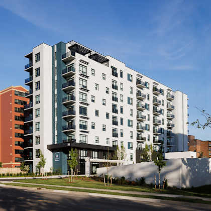 a modern multi-story apartment building with balconies and a mix of white and darker colored facades.