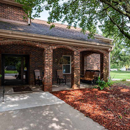 a brick building with a porch and a tree in front.