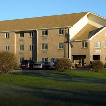 a large building with a flag on top is surrounded by a grassy area and a few cars parked in front.