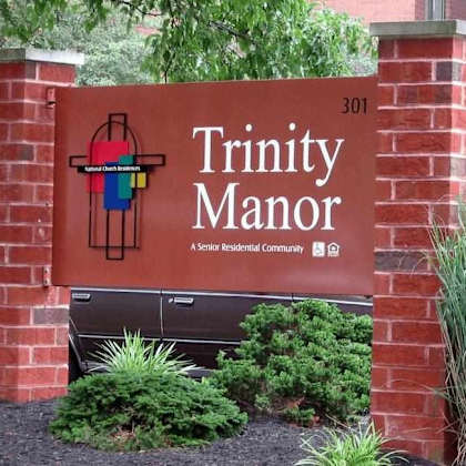a sign for trinity manor, a senior residential community, is displayed in front of a brick wall.