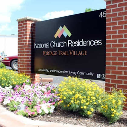 a sign for national church residences portage trail village stands in front of a brick wall.