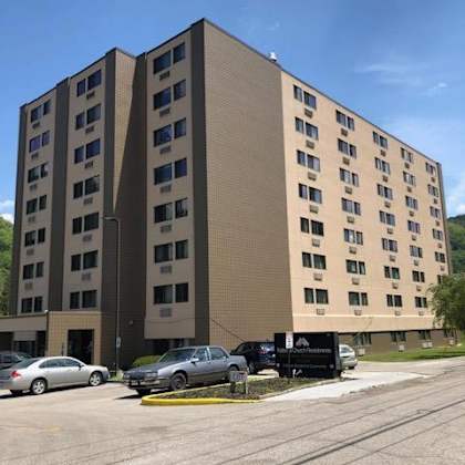 a large tan building with many windows sits next to a parking lot.