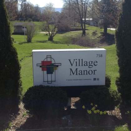 a sign for village manor is shown in front of some trees.