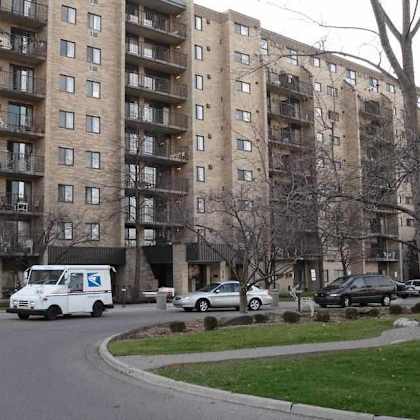a white van with a blue cross on the side is parked on the street in front of a large apartment building.