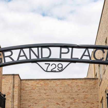 a sign that says grand place 729 is hanging from a black metal frame.