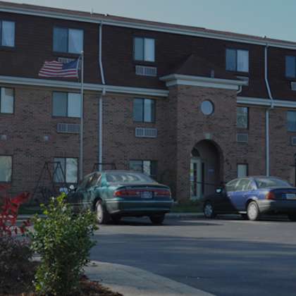 two cars parked in front of a brick building with an american flag on top.