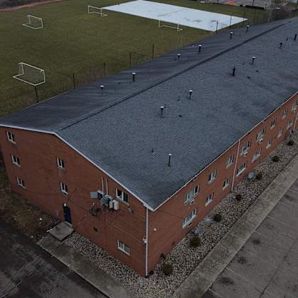 a red brick building with a grey roof is surrounded by a parking lot.