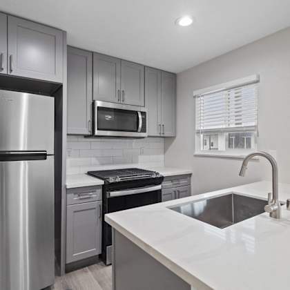 an empty kitchen with stainless steel appliances and white countertops at charle square apartments, costa mesa