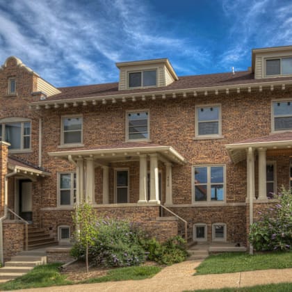 a large, old-style brick house with a front porch and a staircase leading to the entrance.