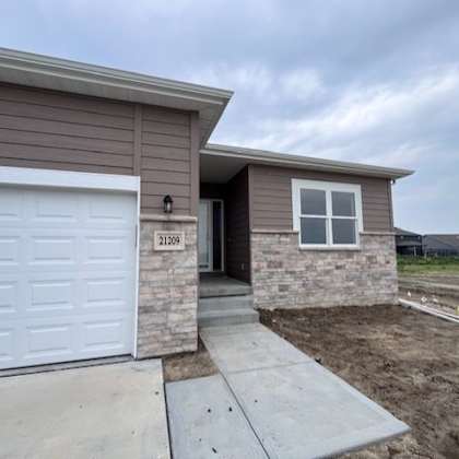 a house with a brown siding and a white garage door is numbered 21209.