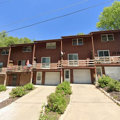a two-story apartment building with a brown exterior and a white car parked in front.