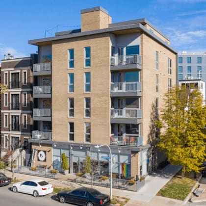 a street view of a residential area with cars parked on the side of the road and apartment buildings in the background.