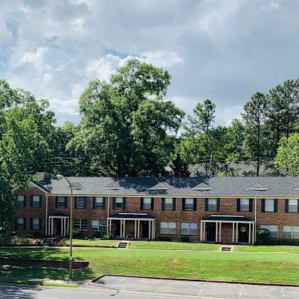 the front of a brick building with a lawn and trees