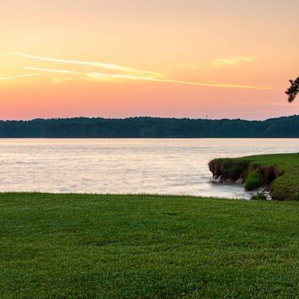 a view of a lake at sunset with grass and trees