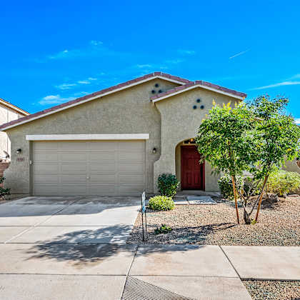 a house with a red door and a garage door is surrounded by a gravel driveway and a small tree.