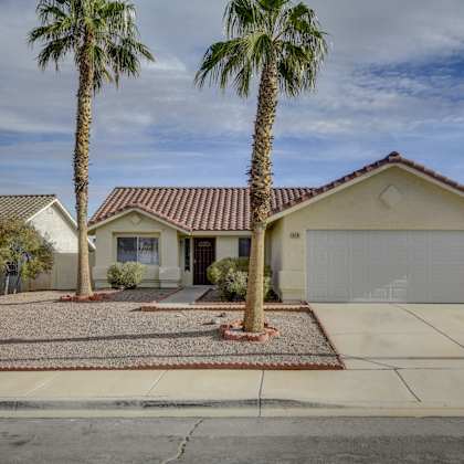 a house with a red tile roof and a white garage door is surrounded by palm trees.