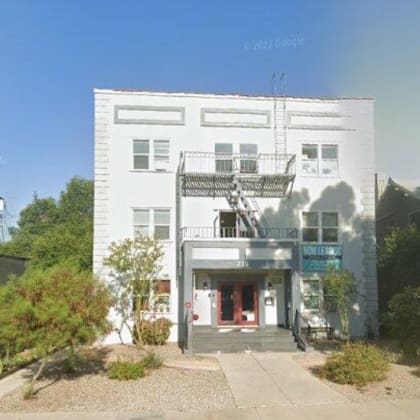 the front of a white building with a balcony and a sidewalk