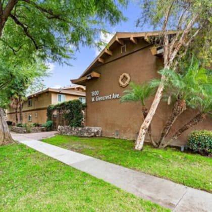 the sidewalk in front of an apartment building with trees and grass