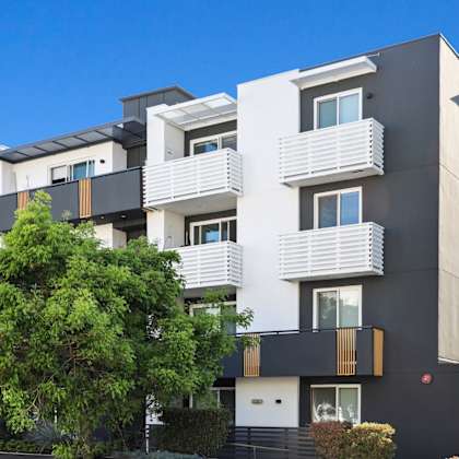 a modern multi-story residential building with balconies and a large tree in front.