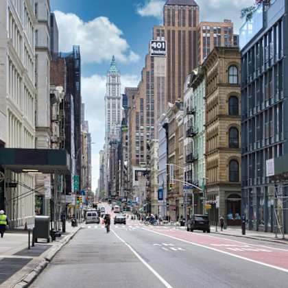 a city street with buildings on both sides and a few pedestrians walking.