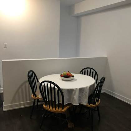 a table with a white cloth and a bowl of fruit on it is surrounded by four chairs.