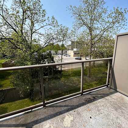 a balcony with a metal railing and a view of a parking lot and trees.
