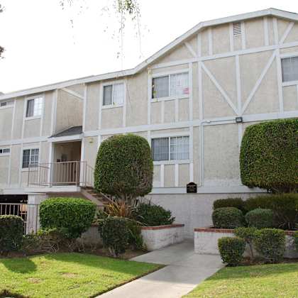 a white building with a balcony and a green bush in front.