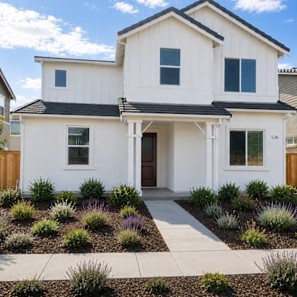 a white two-story house with a black roof and a small front yard with plants.