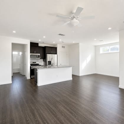 a spacious kitchen and living room with wood flooring and white walls.