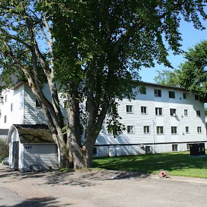 a white building with a garage door is surrounded by trees.