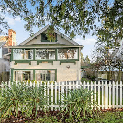 a white picket fence surrounds a green house.