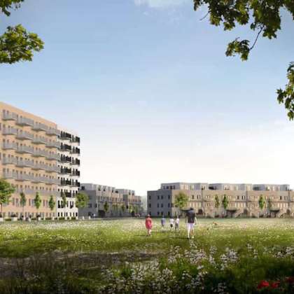 a grassy field with people walking and trees in the foreground with apartment buildings in the background.
