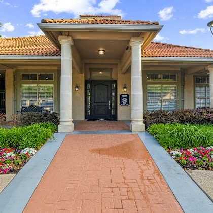 a building with a red tile roof and a black door is surrounded by flowers and a brick pathway.