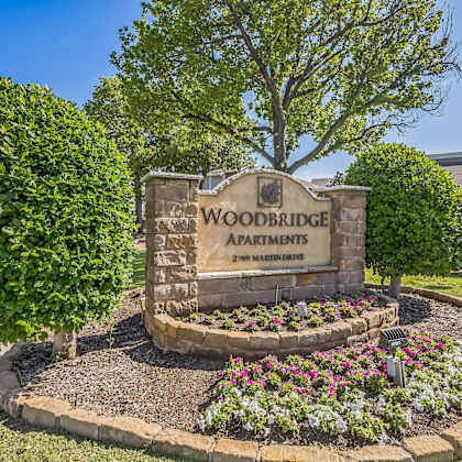 a sign for woodbridge apartments is surrounded by greenery and flowers.