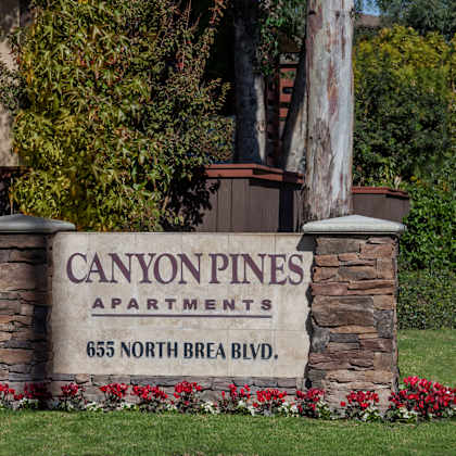 a sign for canyon pines apartments is surrounded by flowers and greenery.