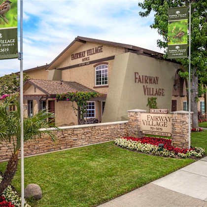 the front of fairway village with a sign and flowers.
