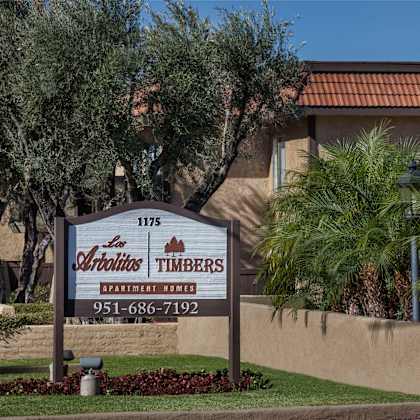 a sign for timbers apartment homes in front of some palm trees.