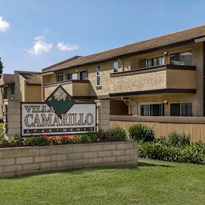 a sign for villa camarillo apartments is in front of a tan building.