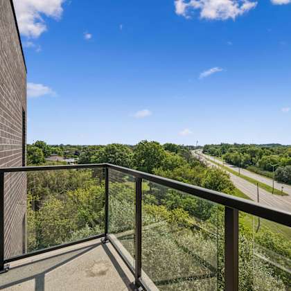 a balcony with a glass railing overlooks a highway and trees.