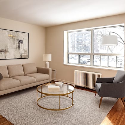 a living room with a beige couch, a grey armchair, a glass coffee table, and a framed artwork on the wall.