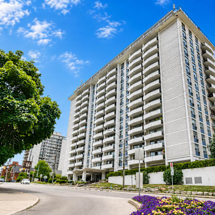 a tall residential building with balconies is surrounded by greenery and a clear blue sky.