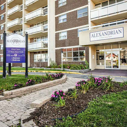 the entrance to the alexandrian apartment complex is shown with a sign and flower bed in front.