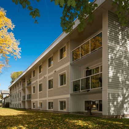 a building with a balcony and a tree with yellow leaves in front of it.