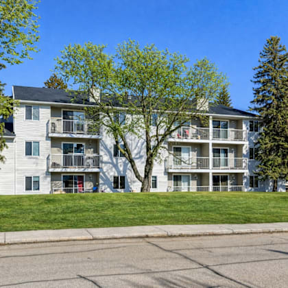 a large white apartment building with balconies and trees in front.