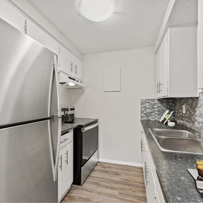 a modern kitchen with a stainless steel refrigerator and black countertops.