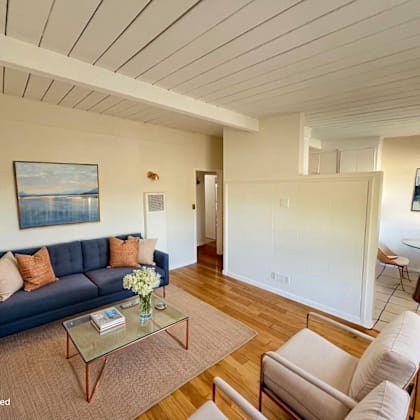 a living room with a blue couch, a glass coffee table, and a painting on the wall.
