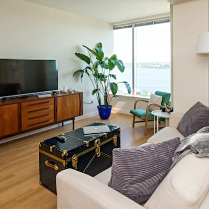 a living room with a white couch, a wooden cabinet, a flat screen tv, a potted plant, and a floor lamp.